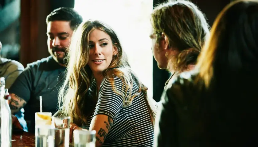 Una mujer sonríe mientras conversa en un bar, quizás aprendiendo como ligar.