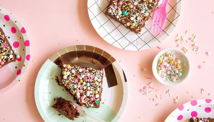 Deliciosos trozos de pastel de chocolate con chispas de colores y estrellas, listos para una merienda de cumpleaños infantil.