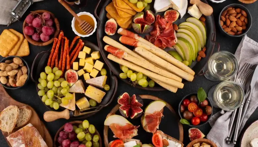 Un delicioso picoteo gourmet con quesos, embutidos, frutas, pan y vino.