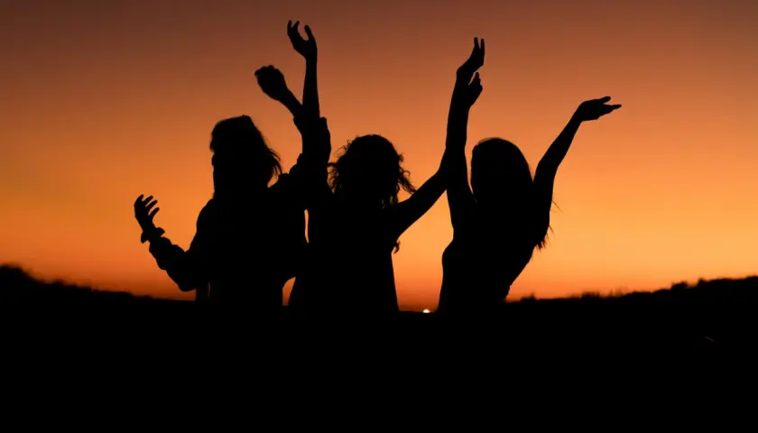 Siluetas de tres amigas bailando al atardecer. Los planes con amigas son los mejores.
