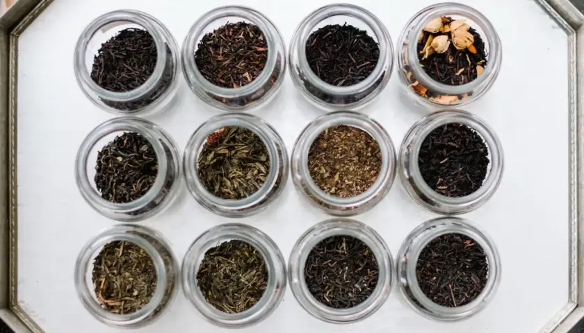 Doce frascos de vidrio muestran diferentes tipos de infusiones, desde tés negros hasta verdes y especiados.