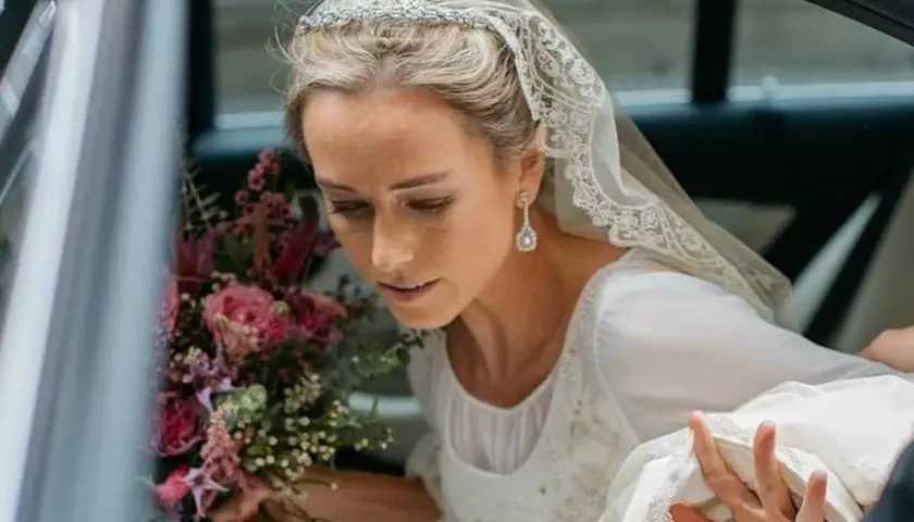Novia con velo de encaje y pendientes largos, un ejemplo de las últimas tendencias en pendientes de novia. Lleva un ramo de rosas.