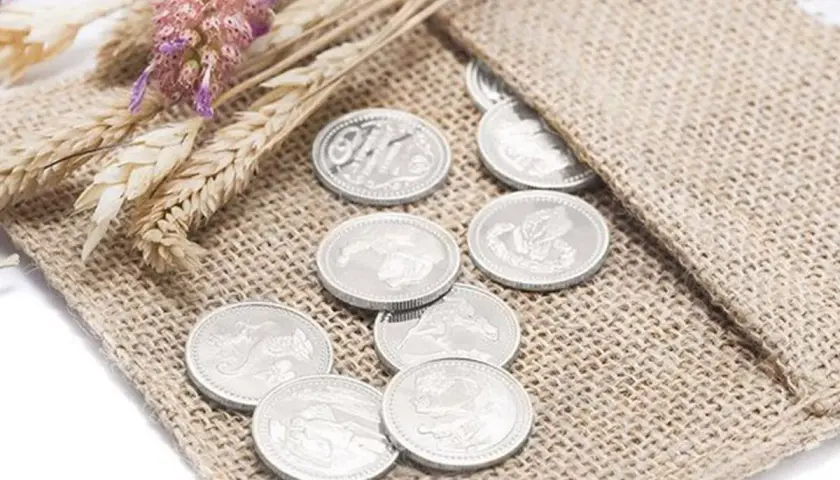 Monedas plateadas, símbolo de prosperidad, junto a espigas y flores secas, representando las arras de boda.