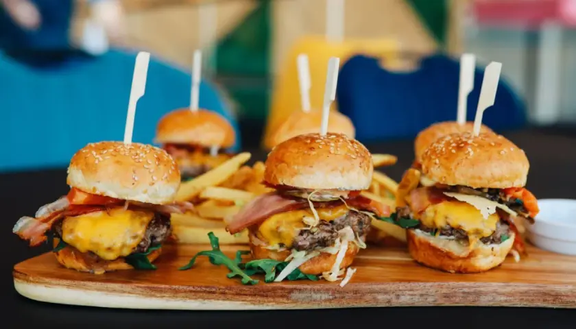 Picoteo comida para cumpleaños en casa: mini hamburguesas jugosas con queso fundido, tocino crujiente y papas fritas. ¡Un festín delicioso!