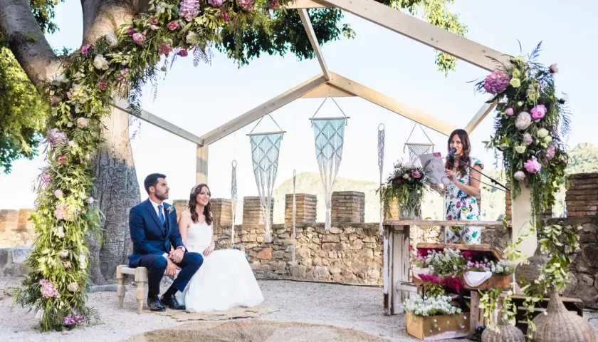 Novia y novio sentados, oficiante leyendo. La decoración floral es exuberante. ¿Cuánto dura una boda civil? Depende de la ceremonia.