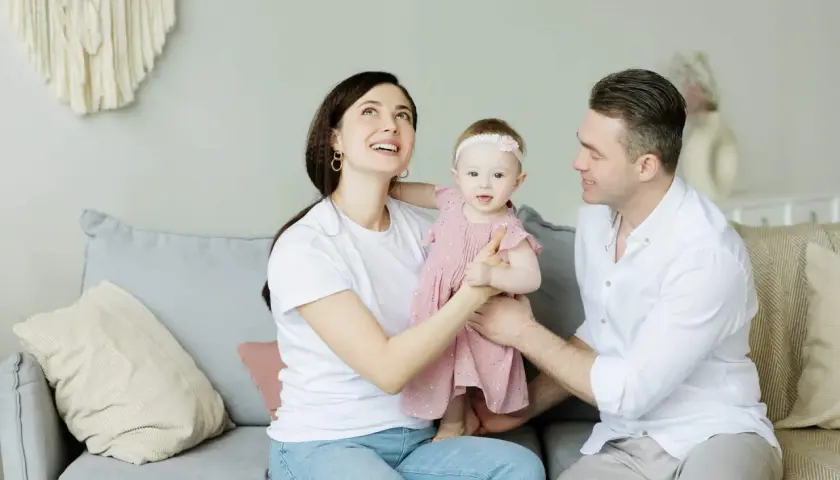 Parejas latinas con hijos, una familia feliz en el sofá. La madre mira hacia arriba con asombro, el padre sonríe a su bebé.