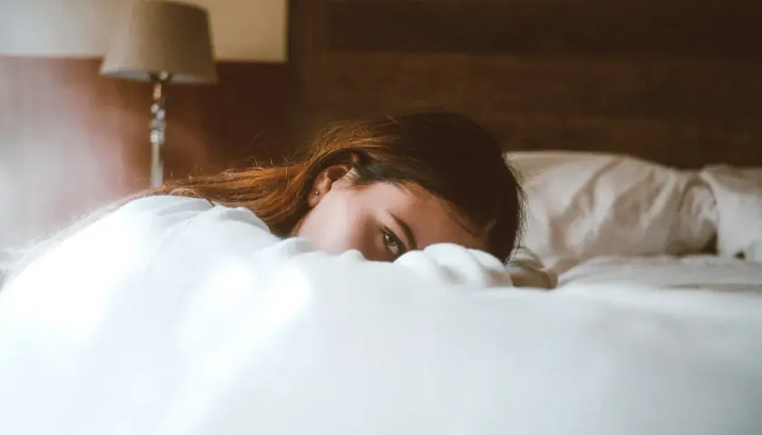 Una mujer yace en la cama, oculta entre las sábanas, con una mirada que evoca la disforia postcoital.