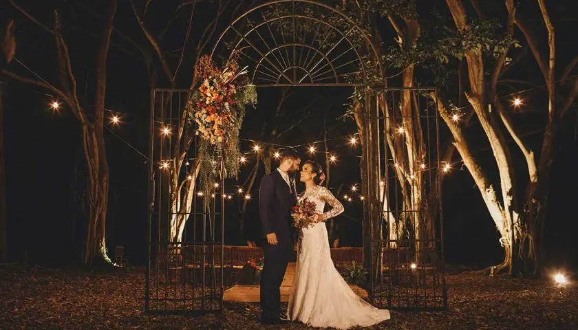 Pareja en un arco adornado con flores, bajo luces de feria. ¿Es una boda, no boda?