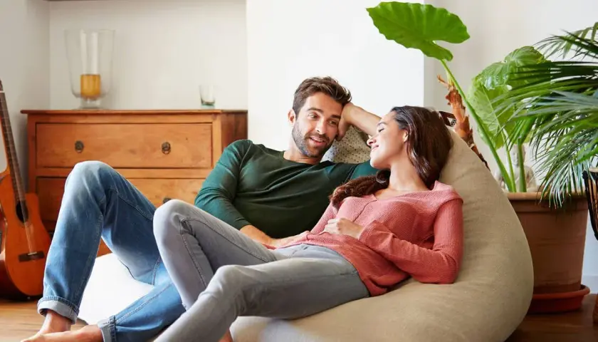 Parejas lat relajadas en un puf, compartiendo un momento íntimo en casa.