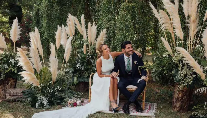 Novios sonriendo en su **boda del año**, rodeados de pampas y vegetación exuberante.