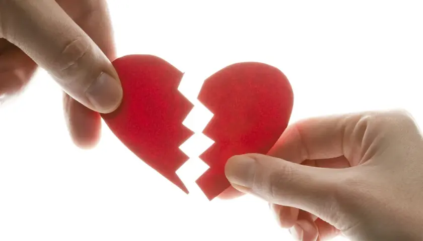 Manos separando un corazón rojo roto, símbolo del mal de amores.