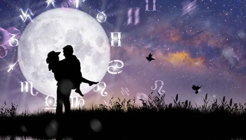 Silueta de pareja abrazada bajo la luna llena, rodeada de símbolos zodiacales. Una escena que evoca la compatibilidad signos zodiaco y el romance cósmico.