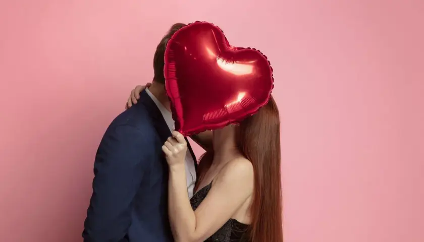 Pareja besándose detrás de un globo rojo en forma de corazón. Ideas románticas para sorprender a tu pareja.