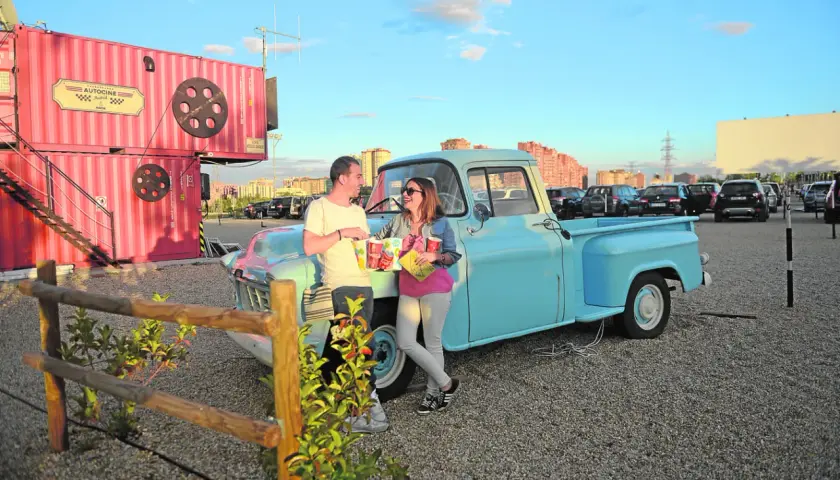 Pareja disfrutando de planes en pareja originales sin dinero en un autocine, apoyados en una camioneta azul, con palomitas y bebidas.