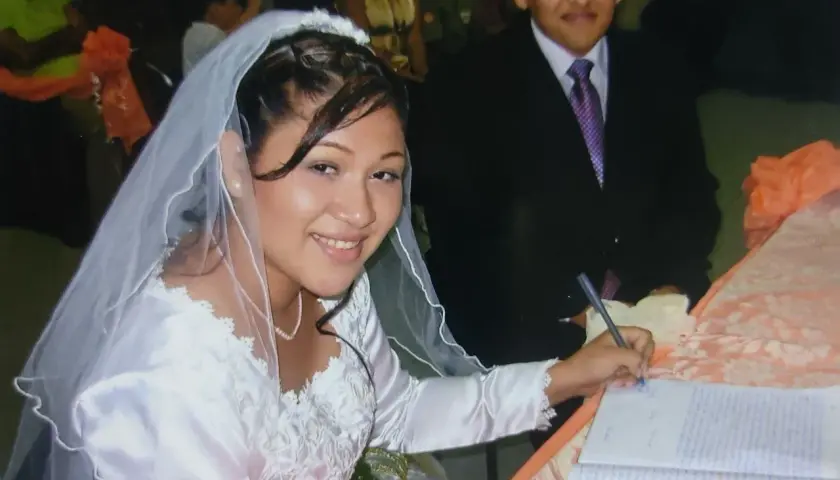 Novia sonriente firma su acta de matrimonio. A su lado, el novio. Celebrando 17 años de casados.