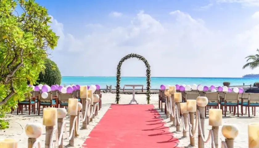 Alfombra roja y sillas decoradas con globos para una hermosa ceremonia de boda en la playa. El mar turquesa y el cielo azul crean el escenario perfecto.