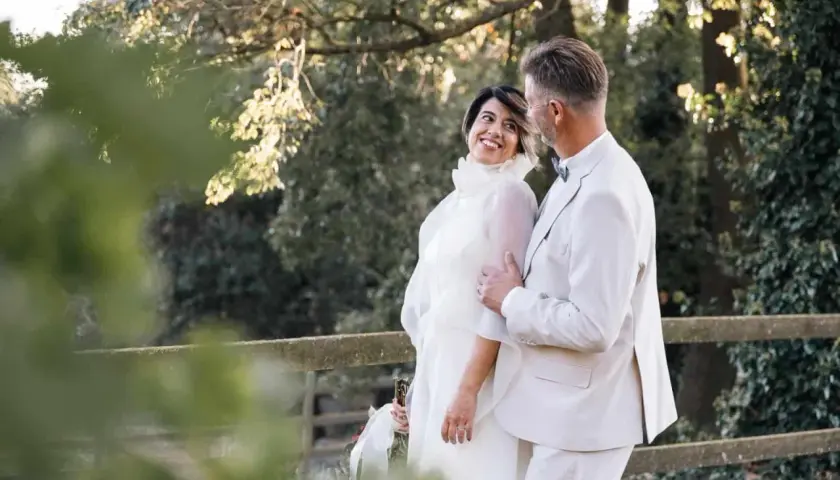 Pareja sonriente en su segunda boda a los 50 años de edad. Ella luce un vestido blanco vaporoso, él un traje claro.