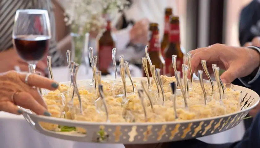 Bandeja con aperitivos individuales, ideal para un coctel de bienvenida de boda. Se ven manos tomando uno.