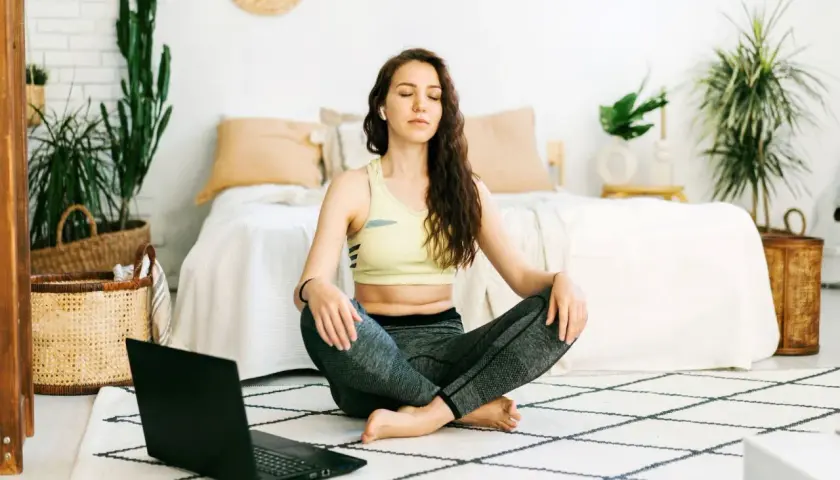 Mujer meditando en posición de loto, aprendiendo técnicas de relajación con un portátil.