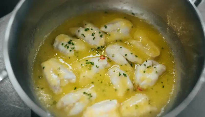 Trozos de bacalao cocinándose en aceite de oliva con ajo y guindilla, listos para la bacalao pil pil receta.