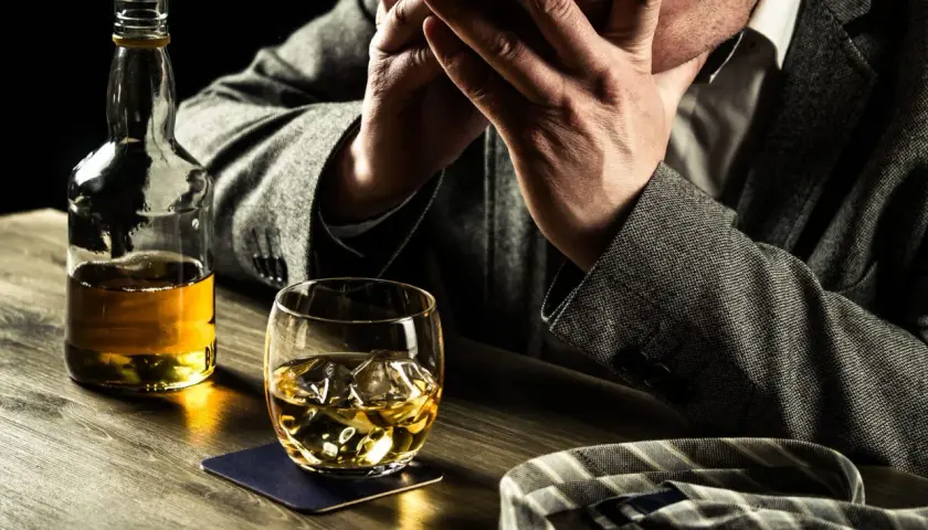 Hombre angustiado con botella y vaso de whisky. Busca remedios caseros para dejar de beber alcohol.