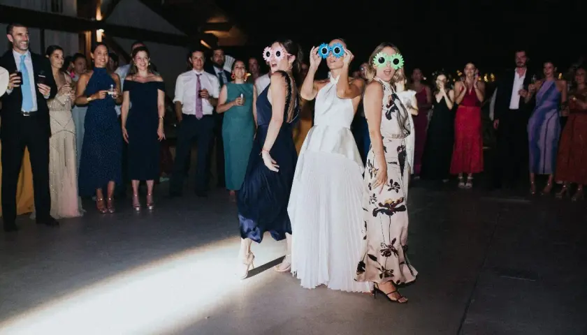 Un grupo de mujeres con gafas divertidas celebra una sorpresa para los novios en una fiesta.