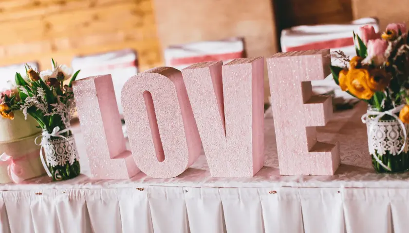 Letras gigantes "LOVE" en rosa brillante, un detalle perfecto para una decoración boda civil sencilla y barata. Flores a los lados.