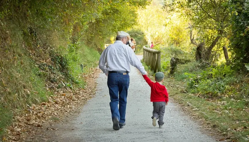 Abuelo y nieto caminan de la mano por un sendero otoñal. Un ejemplo de refranes cortos: "La unión hace la fuerza".