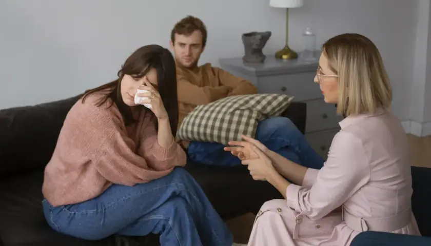Una pareja discute temas de conversación difíciles con un terapeuta. La mujer llora mientras el hombre la mira.