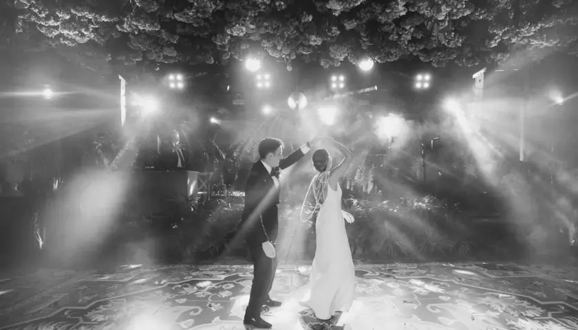 Novios bailando su primera canción, rodeados de luces y vegetación exuberante. La pista de baile decorada con un patrón intrincado.