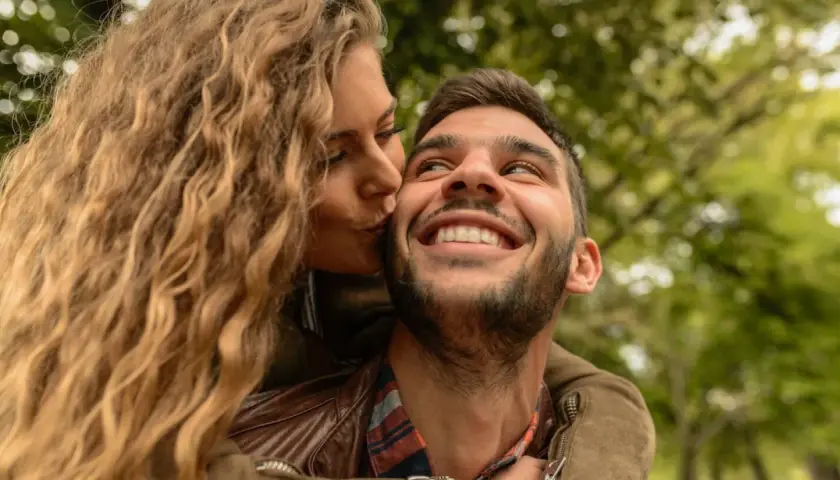 Una mujer rubia besa en la mejilla a un hombre sonriente. Las reglas de pareja se basan en el amor y la confianza.