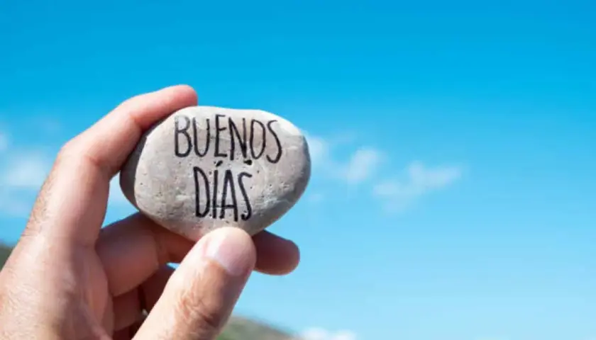 Un cariñoso saludo de buenos días alegres, escrito en una piedra sostenida contra un cielo azul brillante.