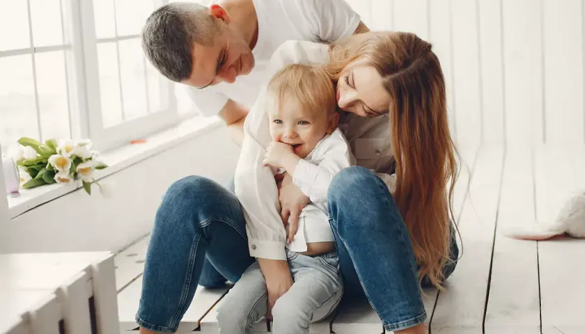 Padres abrazando a su hijo, creando un ambiente de apego seguro. El niño sonríe, rodeado de amor y protección.
