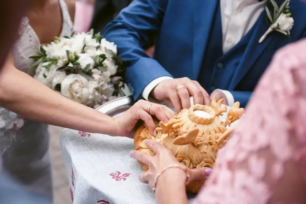 Manos de novios tocando un pan decorado, parte de rituales de boda en diferentes culturas.