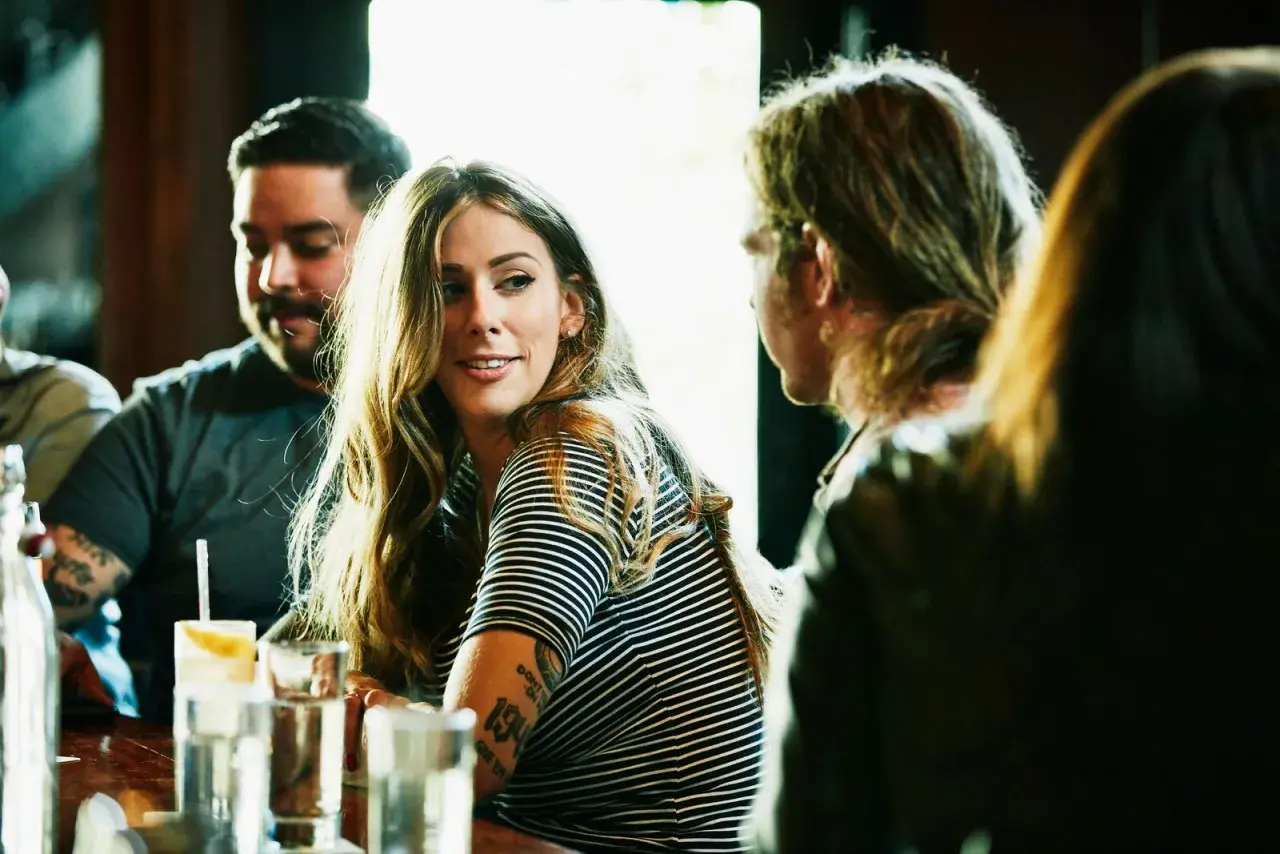 Una mujer sonríe mientras conversa en un bar, quizás aprendiendo como ligar.