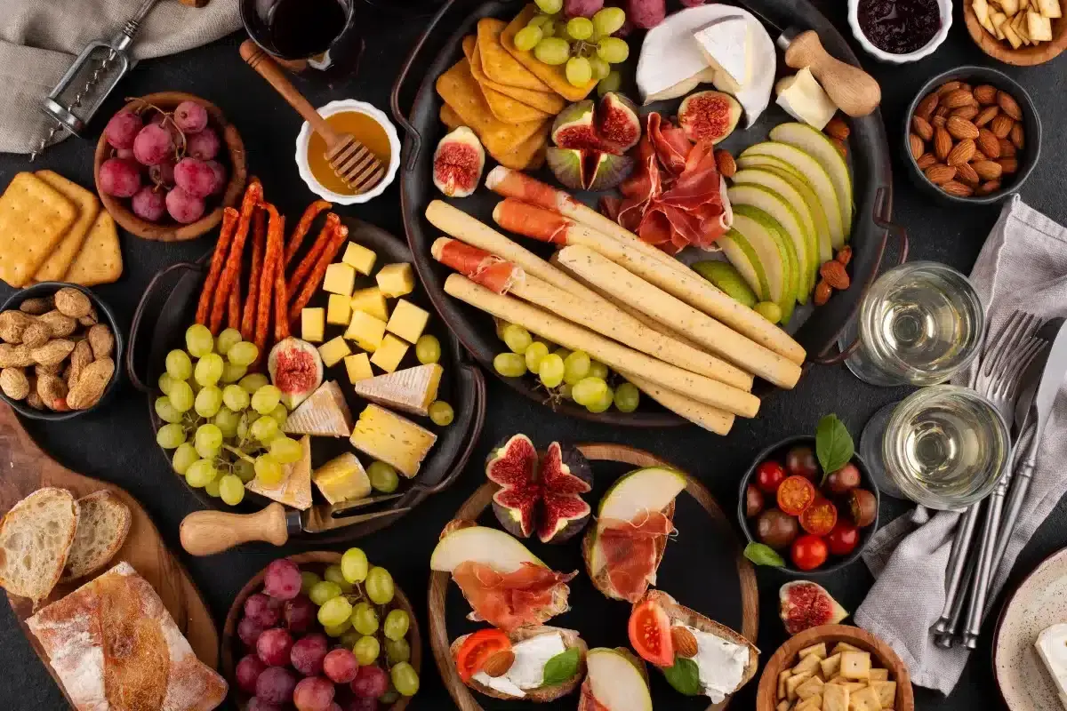 Un delicioso picoteo gourmet con quesos, embutidos, frutas, pan y vino.