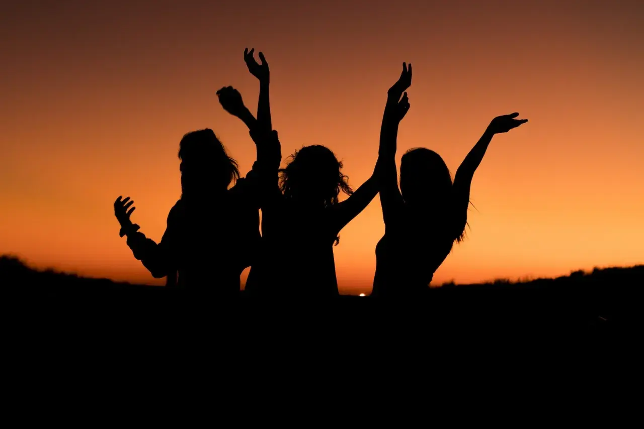Siluetas de tres amigas bailando al atardecer. Los planes con amigas son los mejores.