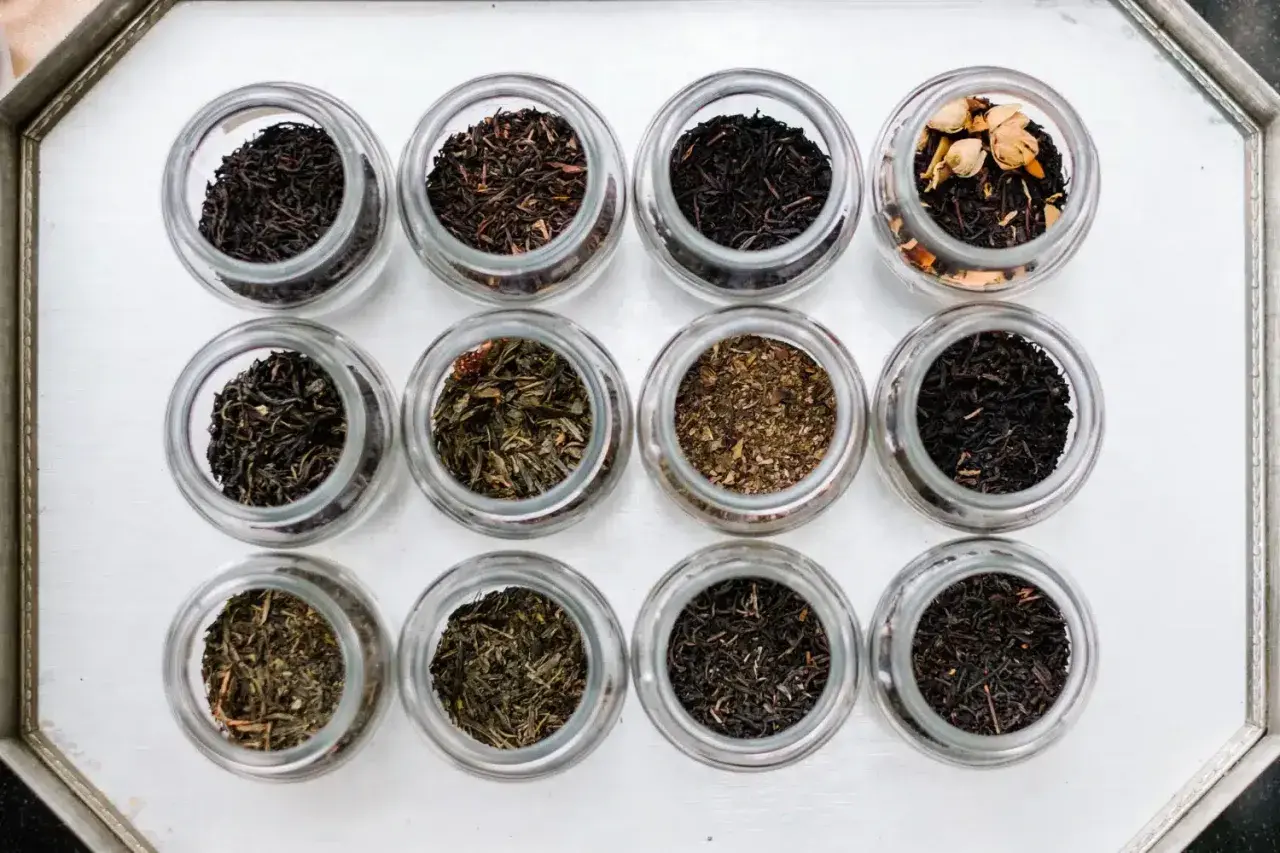 Doce frascos de vidrio muestran diferentes tipos de infusiones, desde tés negros hasta verdes y especiados.