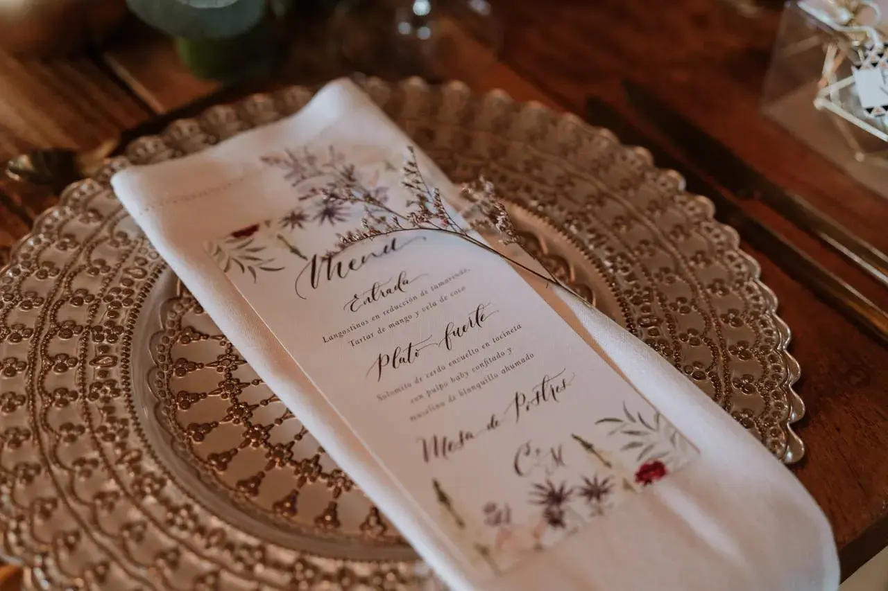 Un elegante menú de boda con caligrafía floral detalla los platos: langostinos, solomito de cerdo y mesa de postres.