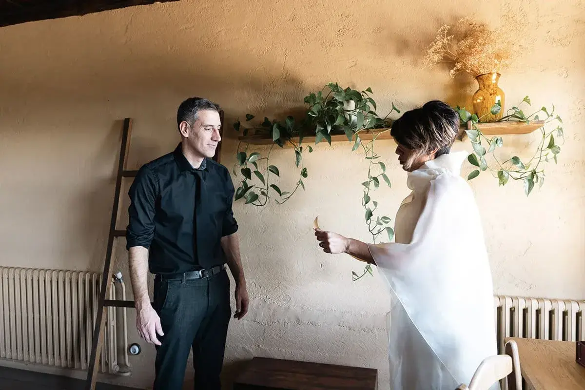 Pareja intercambiando un detalle, quizás una nota, como parte de sus ideas para aniversario. Él, de negro; ella, de blanco.