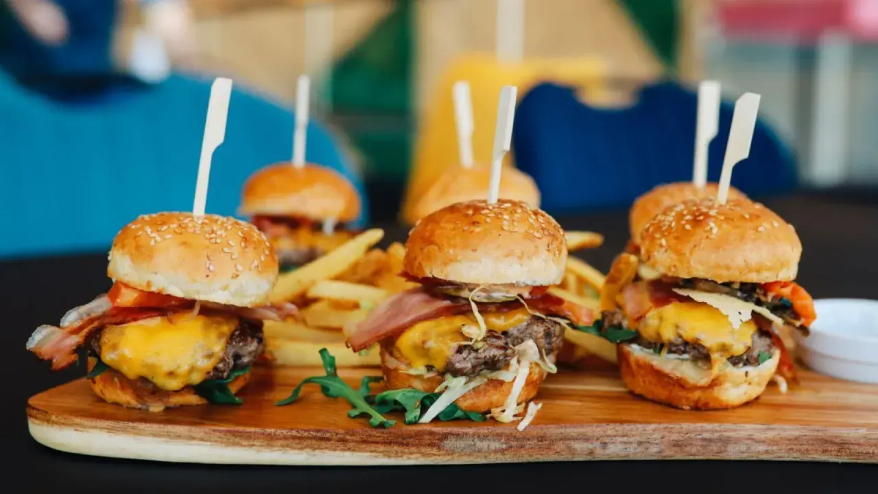 Picoteo comida para cumpleaños en casa: mini hamburguesas jugosas con queso fundido, tocino crujiente y papas fritas. ¡Un festín delicioso!