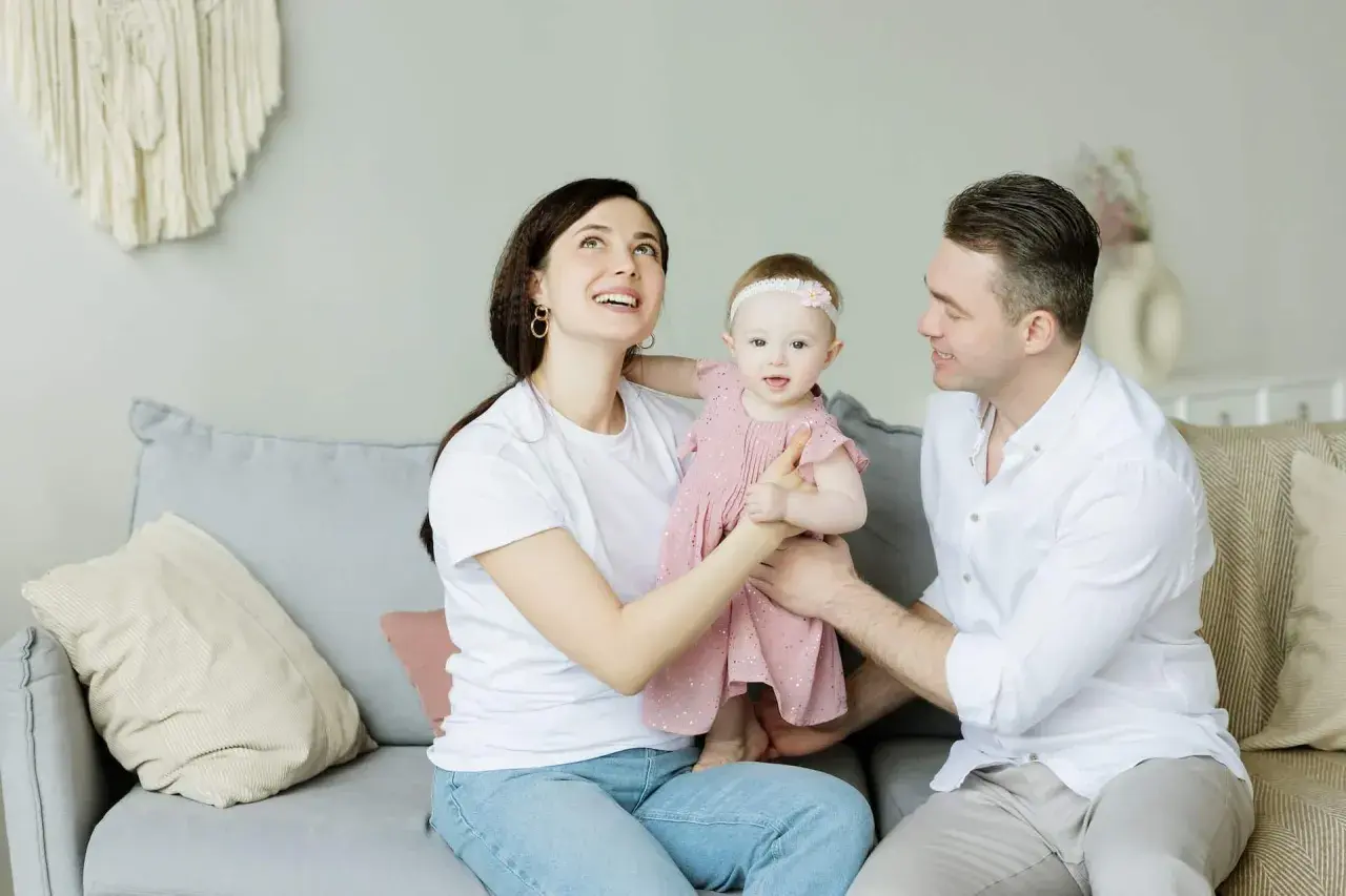 Parejas latinas con hijos, una familia feliz en el sofá. La madre mira hacia arriba con asombro, el padre sonríe a su bebé.