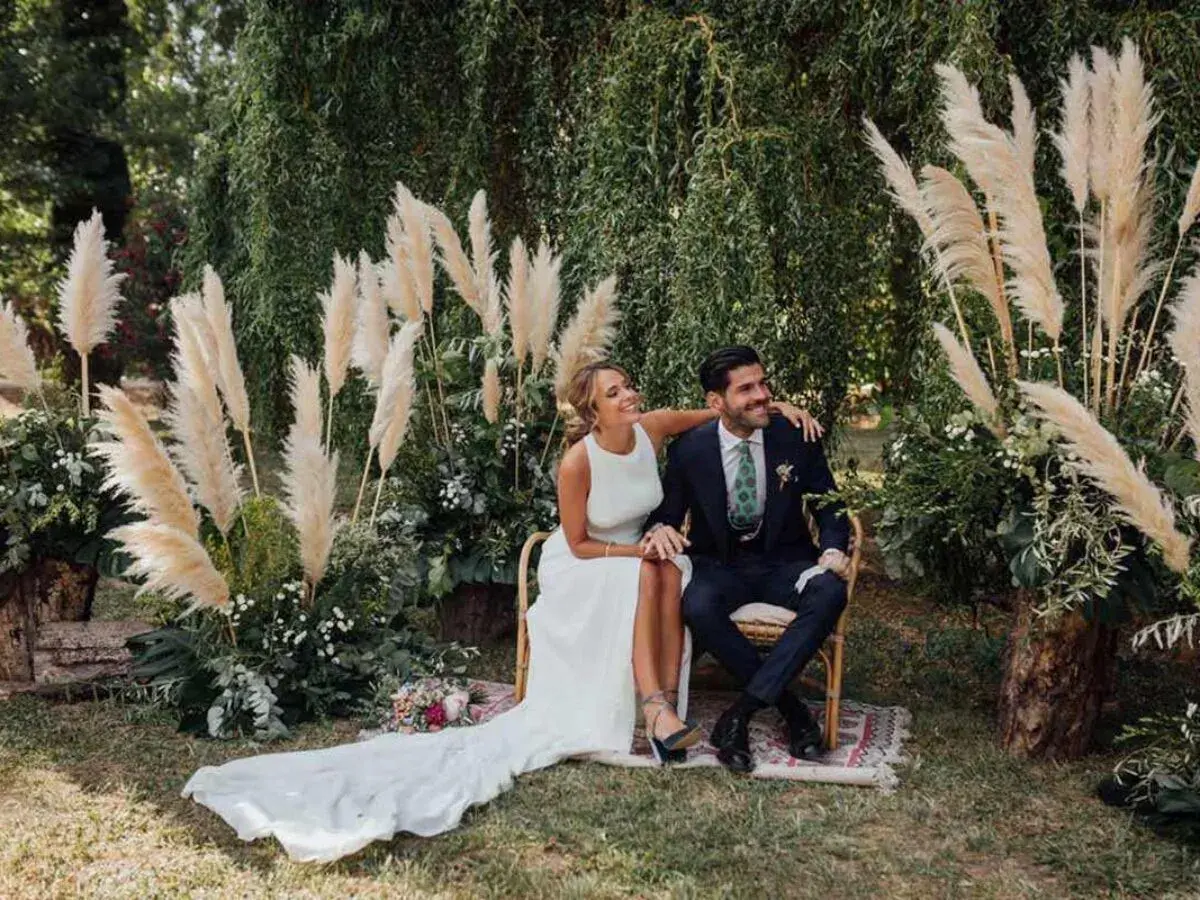 Novios sonriendo en su **boda del año**, rodeados de pampas y vegetación exuberante.