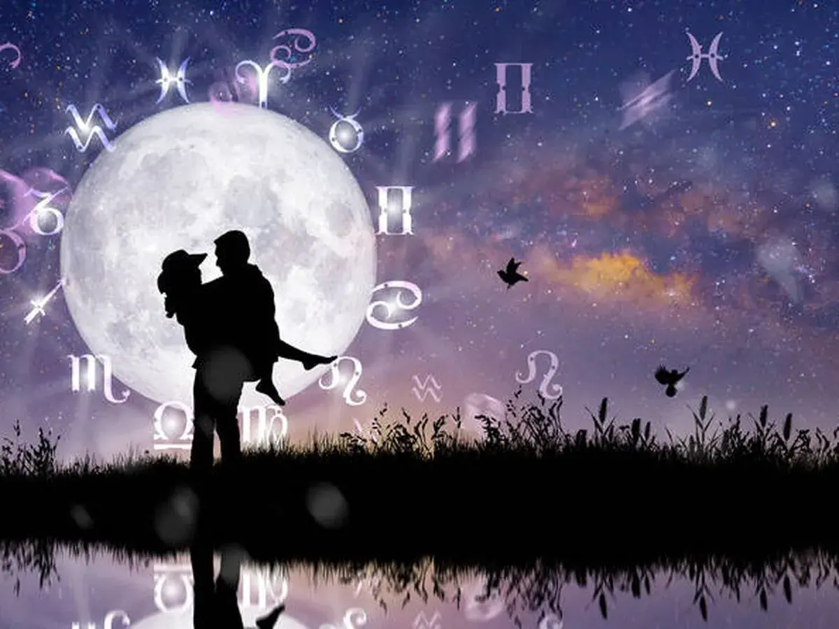 Silueta de pareja abrazada bajo la luna llena, rodeada de símbolos zodiacales. Una escena que evoca la compatibilidad signos zodiaco y el romance cósmico.