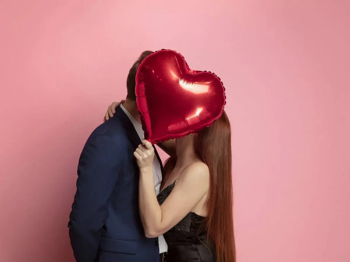 Pareja besándose detrás de un globo rojo en forma de corazón. Ideas románticas para sorprender a tu pareja.