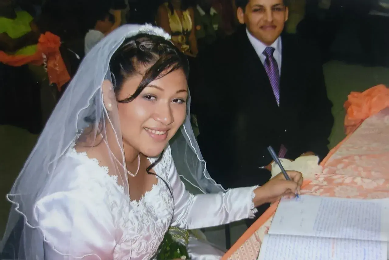 Novia sonriente firma su acta de matrimonio. A su lado, el novio. Celebrando 17 años de casados.