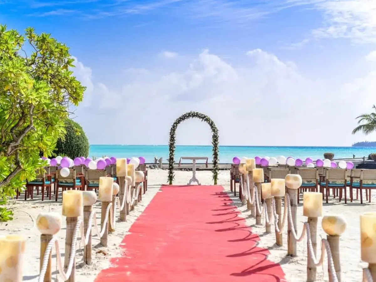 Alfombra roja y sillas decoradas con globos para una hermosa ceremonia de boda en la playa. El mar turquesa y el cielo azul crean el escenario perfecto.