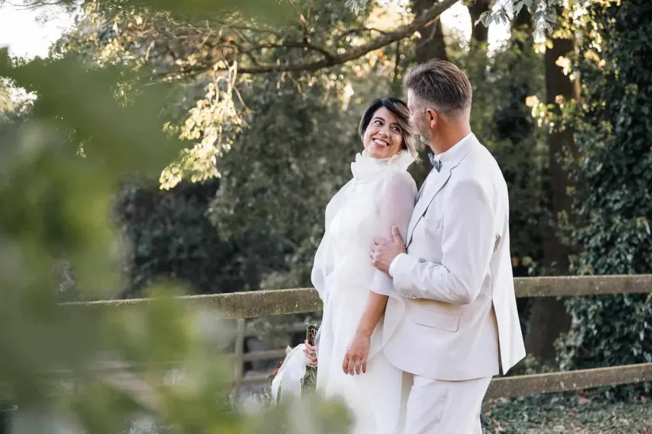 Pareja sonriente en su segunda boda a los 50 años de edad. Ella luce un vestido blanco vaporoso, él un traje claro.
