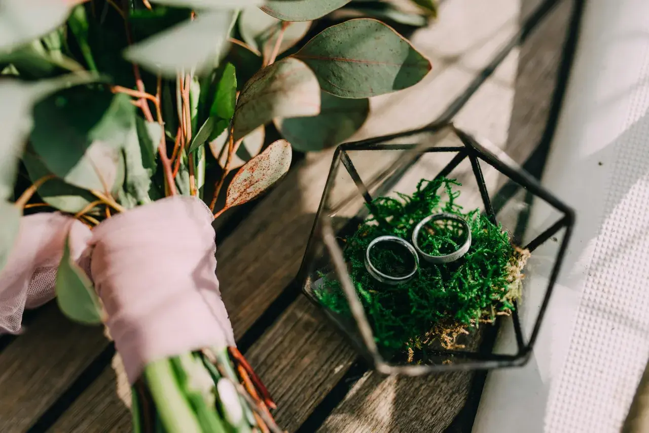 Anillos de boda en musgo dentro de un terrario de vidrio, junto a un ramo con flores y velo rosa. Celebrando un aniversario boda 5 años.