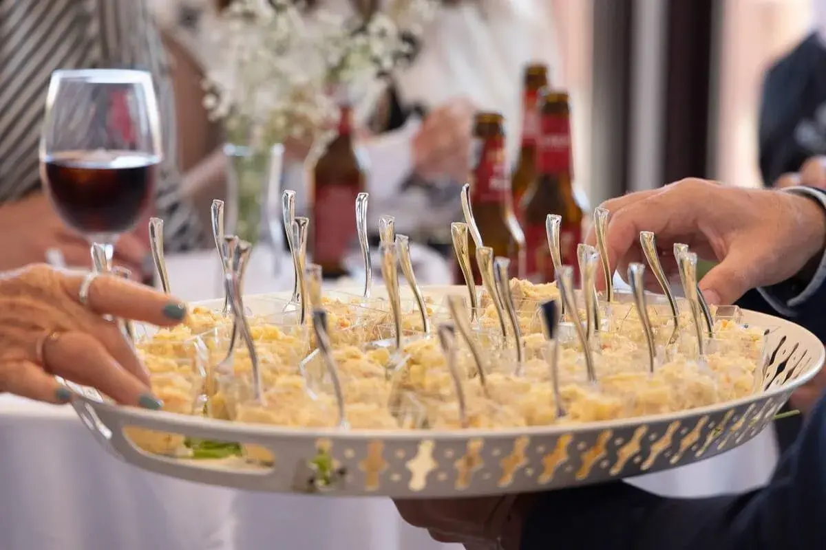 Bandeja con aperitivos individuales, ideal para un coctel de bienvenida de boda. Se ven manos tomando uno.